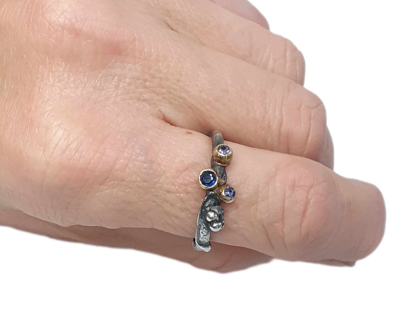 
                  
                    Dieser Ring wurde oxidiert, um den Kontrast zwischen Gold und Silber zu verstärken. Die Steine sind in einer Palette von dunkelblau, lila und lavendel gehalten. Der 3 mm große Stein ist ein Saphir, während die beiden anderen Steine Iolith sind. Wie immer ist das Gold und Silber recycelt.
                  
                