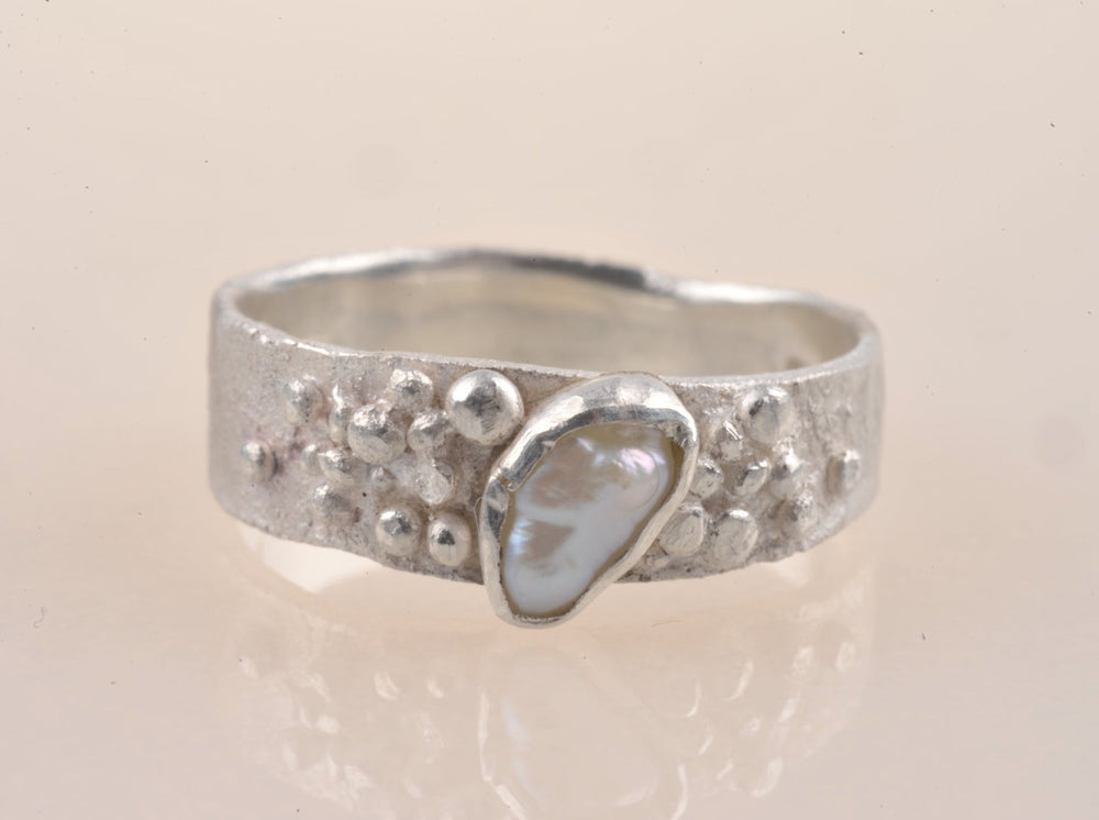 Für Neptuns Töchter könnte dieser Granulatring für Ariel sein. Einzigartig in recyceltem Silber, ist das Band sorgfältig mit einzeln gelöteten, handgefertigten Granulaten verziert, die eine leuchtende, ovale Süßwasserperle umgeben.  Der Ring ist super bequem, da er hinten von 6 mm auf 4 mm abfällt und nur 1 mm dick ist. Der Ring ist eine deutsche Größe 19 (59mm Fingerumfang). 