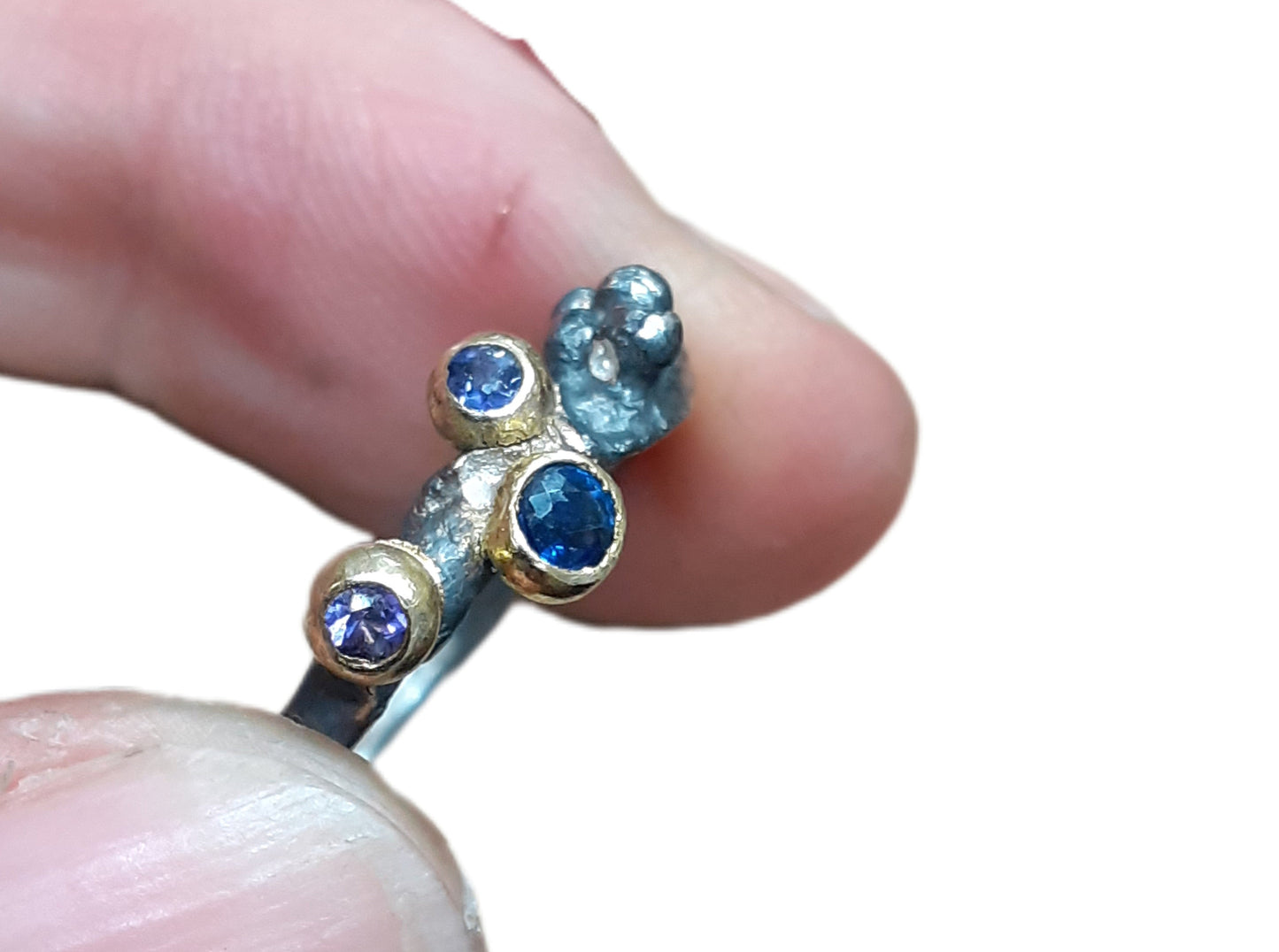 
                  
                    Dieser Ring wurde oxidiert, um den Kontrast zwischen Gold und Silber zu verstärken. Die Steine sind in einer Palette von dunkelblau, lila und lavendel gehalten. Der 3 mm große Stein ist ein Saphir, während die beiden anderen Steine Iolith sind. Wie immer ist das Gold und Silber recycelt.
                  
                