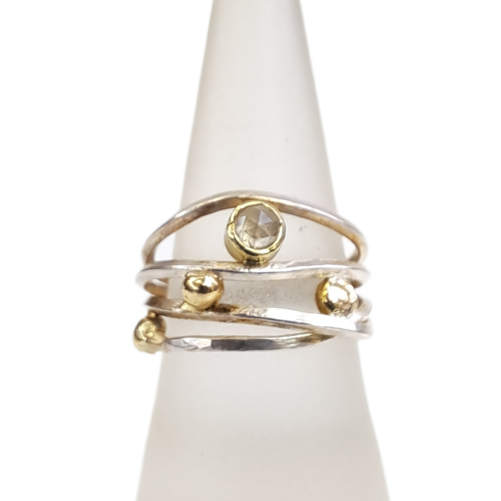 
                  
                    Ein schimmernder 0,3-karätiger Diamant in Zinntönen ist das Herzstück dieses Rings. Inspiriert von den kreisenden Bewegungen des Himmels, kreisen kleine Kugeln aus 14-karätigem Gold zwischen Silberbändern um den schimmernden Diamanten.  An seiner breitesten Stelle ist der Ring 13 mm breit und verjüngt sich auf 4,5 mm für einen angenehmen Tragekomfort.  Ringgröße 54,5
                  
                