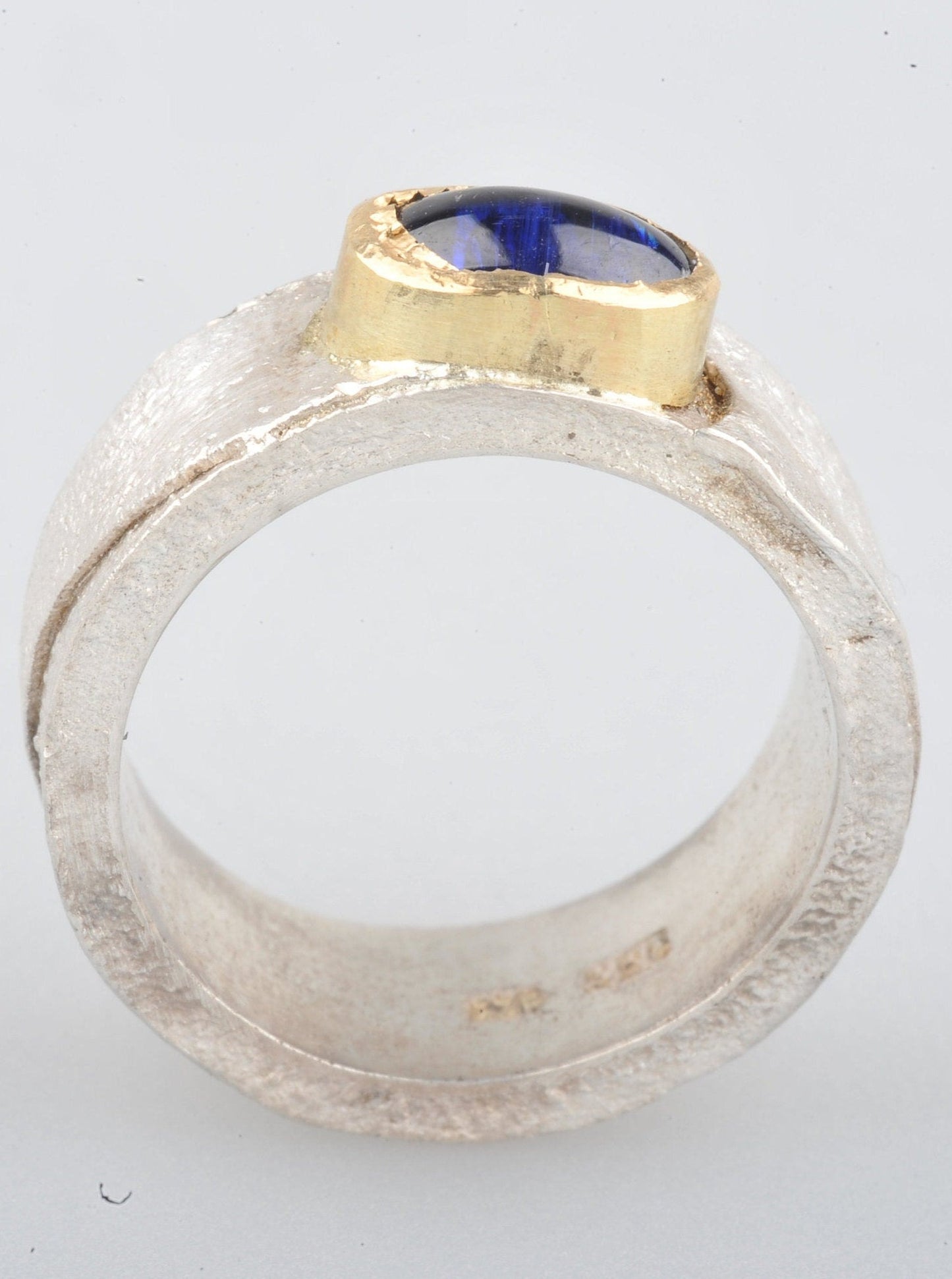 
                  
                    Dieser Ring hat ein schönes Gewicht. Das Band ist 8 mm breit und 2 mm dick. Die Oberfläche wurde retikuliert (ich bringe die Oberfläche des Silbers zum Schmelzpunkt und lasse sie abkühlen. Dies wird mehrmals wiederholt, bis ich mit der Oberflächenstruktur zufrieden bin), während die Innenseite des Bandes glatt und poliert ist. Der Cyanit hat ein wunderschönes tiefes Blau.
                  
                