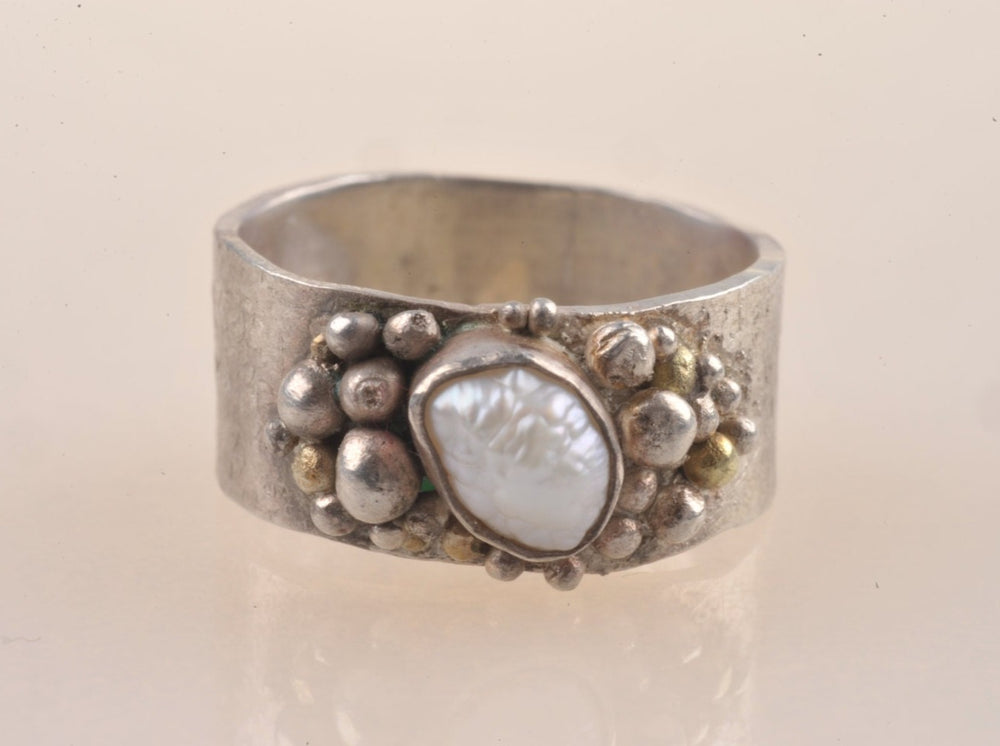 Dieser Ring aus Echtsilber ist mit Gold- und Silberkörnung texturiert. Ich nenne diese Serie meine "Neptun - Ringe", weil sie von den Fingern einer Meerjungfrau stammen könnten.  Der Ring ist 8 -9 mm breit (die Ränder sind nicht gerade, sondern haben sanft geschwungene Kurven) und 1 mm dick. Er ist visuell üppig und gleichzeitig leicht auf dem Finger. Die prächtige Perle schimmert in einem milden Pink und misst 7,5 x 6 mm. Ich habe das Band von Hand texturiert, der Muster erinnert an Schuppen.